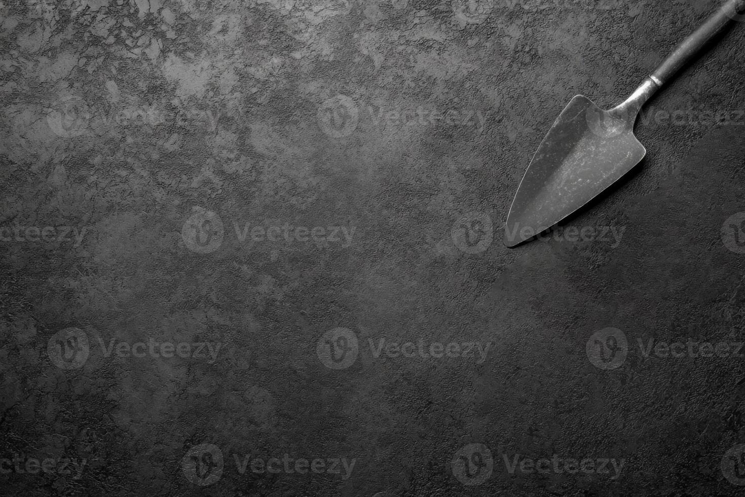 Worn Metal Trowel with a Wooden Handle on a Dark Textured Surface photo