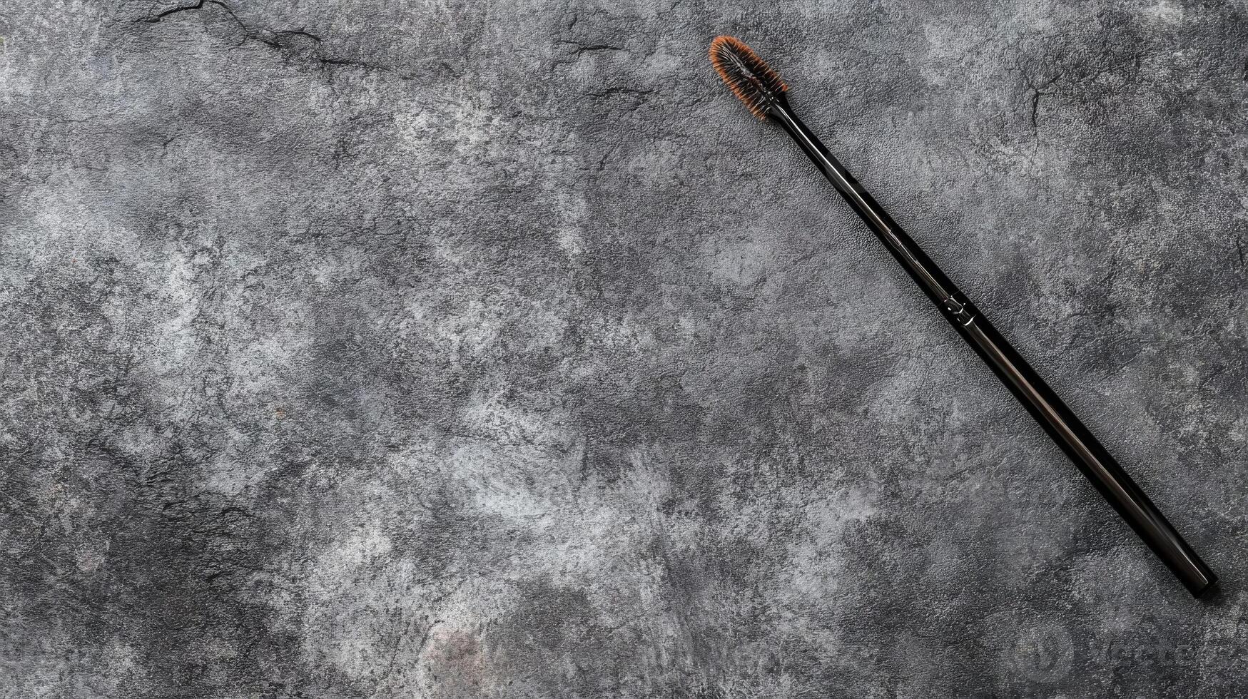 Black Mascara Wand with Brown Bristles on a Textured Gray Surface photo