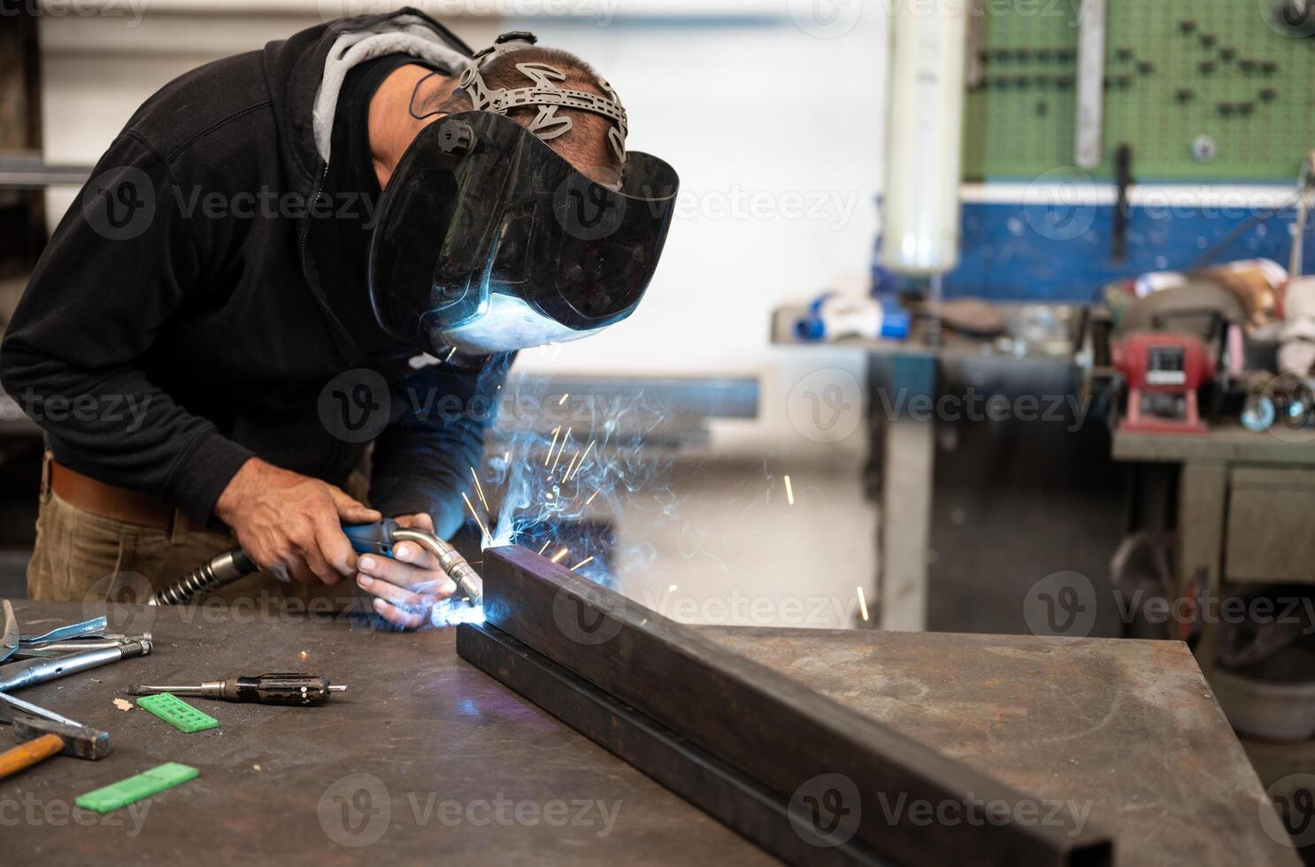 Spectacular conceptual image of a blacksmith busy using the welding machine. Sparks and smoke flash from the tip of the soldering iron. Blurred background. Welding, repair, work concept. Copy space photo