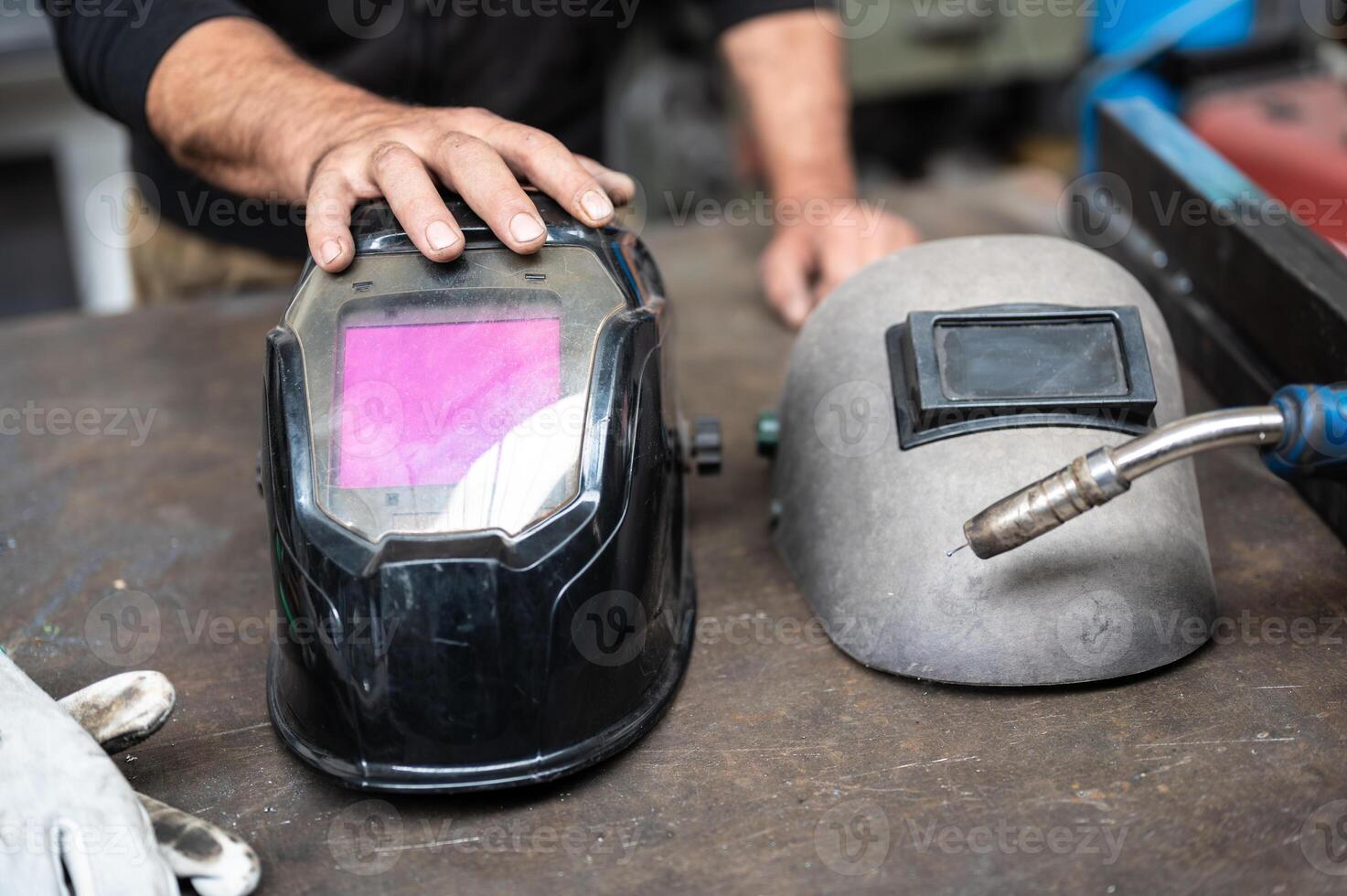 A very strong conceptual image on workplace safety, the strong hand of a worker rests on a modern welder's helmet. On the sides a work glove and the tip of the welding machine. photo
