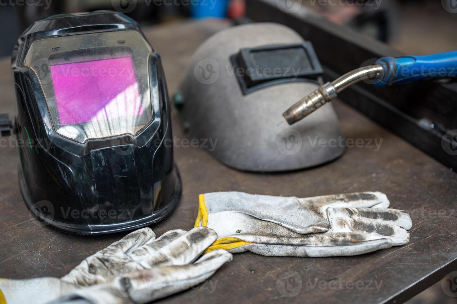 A conceptual image about safety at work, a modern welding helmet and a vintage one next to it. On the sides a work glove and the tip of the welding machine. photo