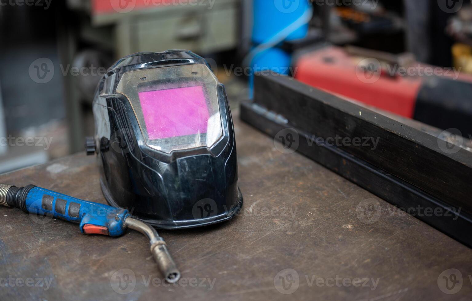 Close-up on the welding helmet, next to the left the welding gun. On the right two welded metal bars. Conceptual image of work, metalworking, craftsmanship. Copy space. photo