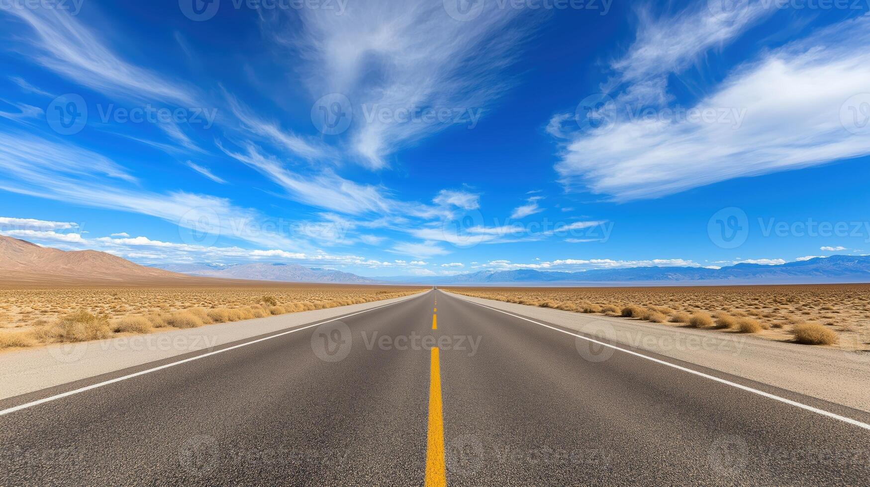 Expansive Open Desert Road Under Bright Blue Sky with Wispy Clouds and Mountain Range in the Distance photo