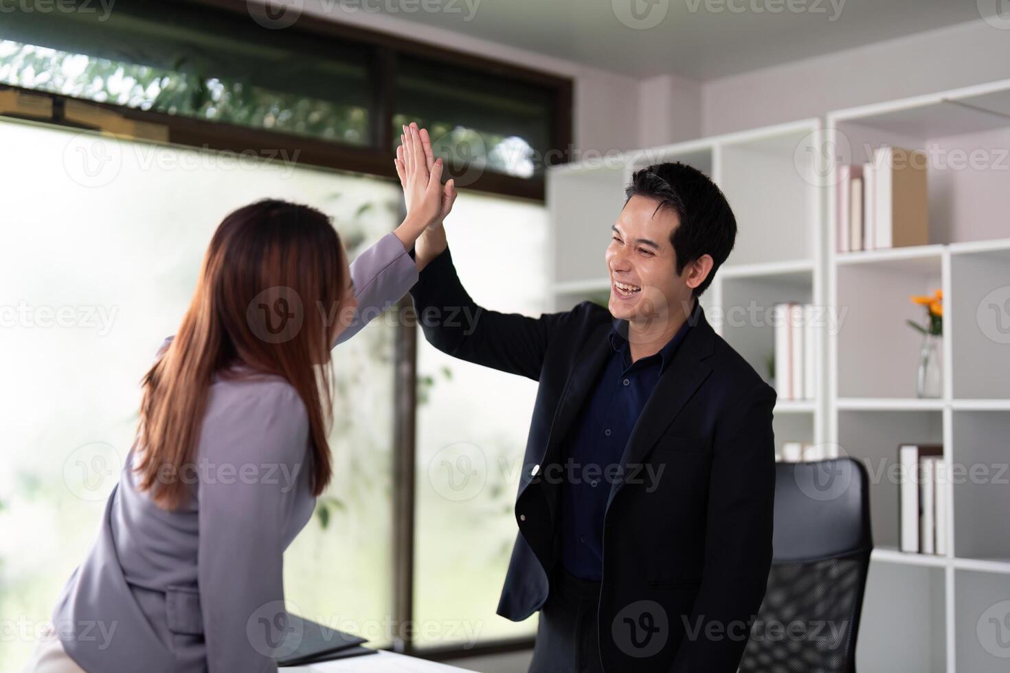 Celebration and Team Dynamics. Two colleagues exchanging high-fives in a vibrant office atmosphere. photo