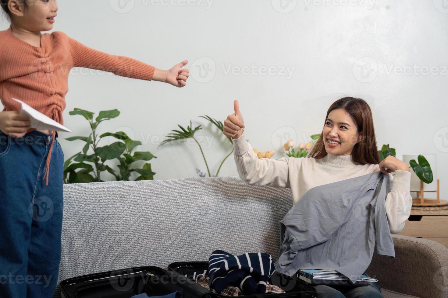 Family Packing and Expression. A little girl gives a thumbs up while helping her mother select clothes for their trip. photo