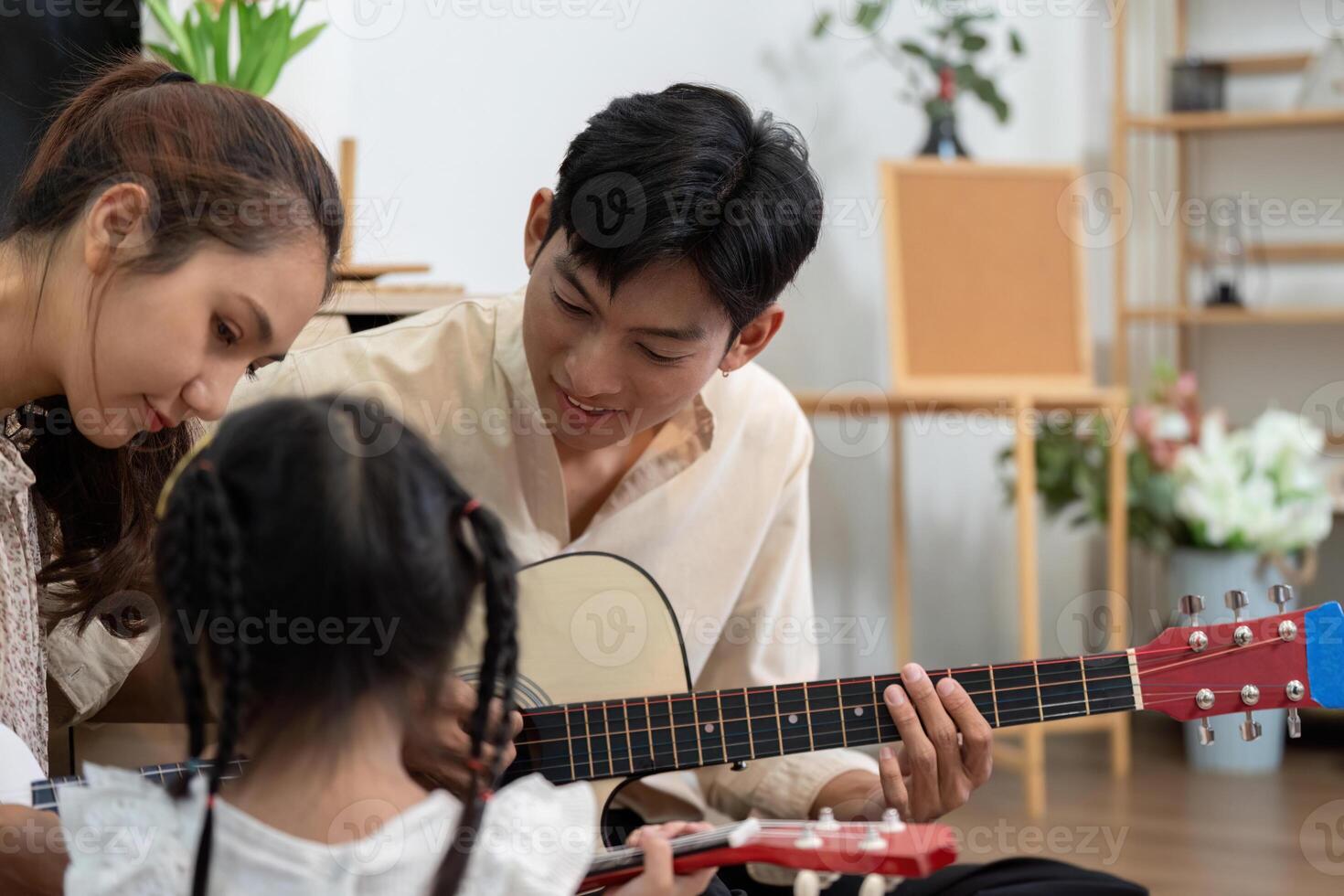 Home Music Lessons and Family Fun. A little girl learning to play guitar surrounded by her supportive parents. photo