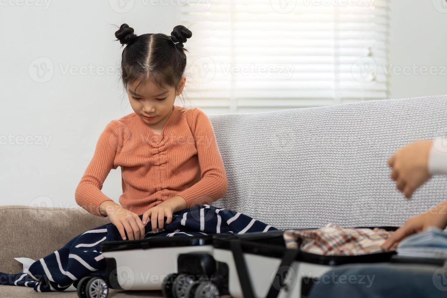 Travel Preparation and Family Bonding. A young girl eagerly engages in packing her suitcase, excitedly folding her clothes with a family member. photo