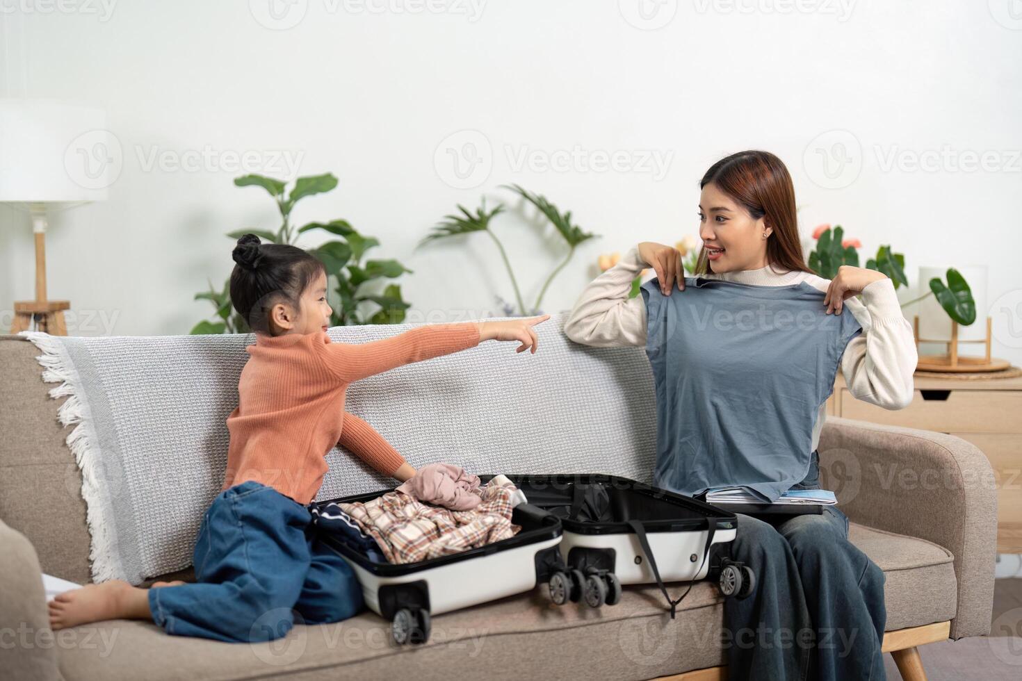 Travel Planning and Cooperation. A girl excitedly points at clothes while sharing a packing moment with her mother. photo