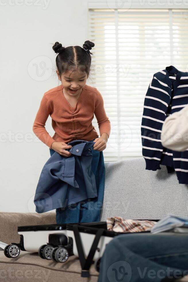 Excitement for Travel and Family Moments. A little girl organizing clothes while packing her suitcase, showcasing joy and anticipation for the upcoming trip. photo