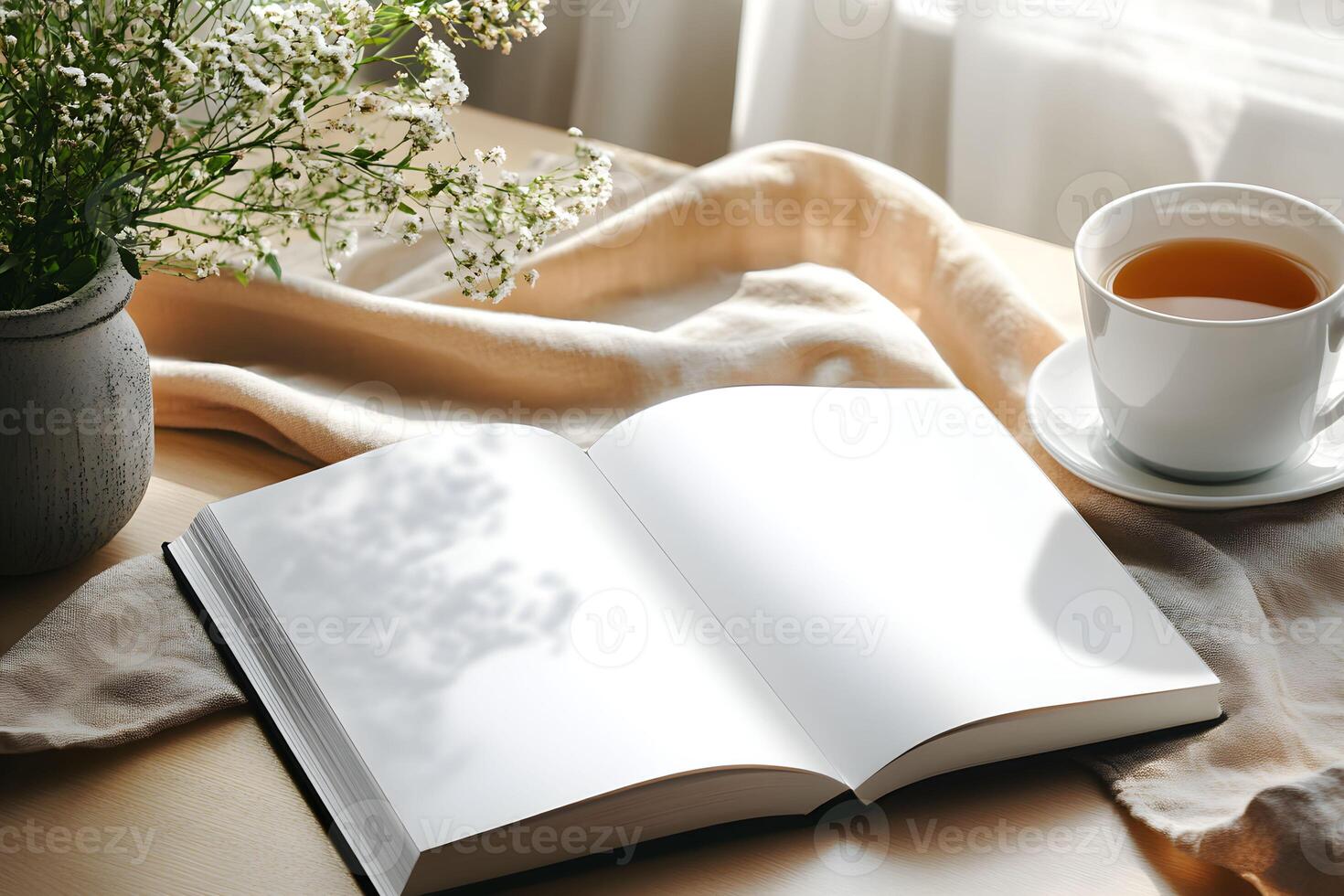 Empty book for mockup with blank pages beside a cup of tea and a vase of flowers on a wooden table in a bright, cozy indoor setting during the afternoon photo