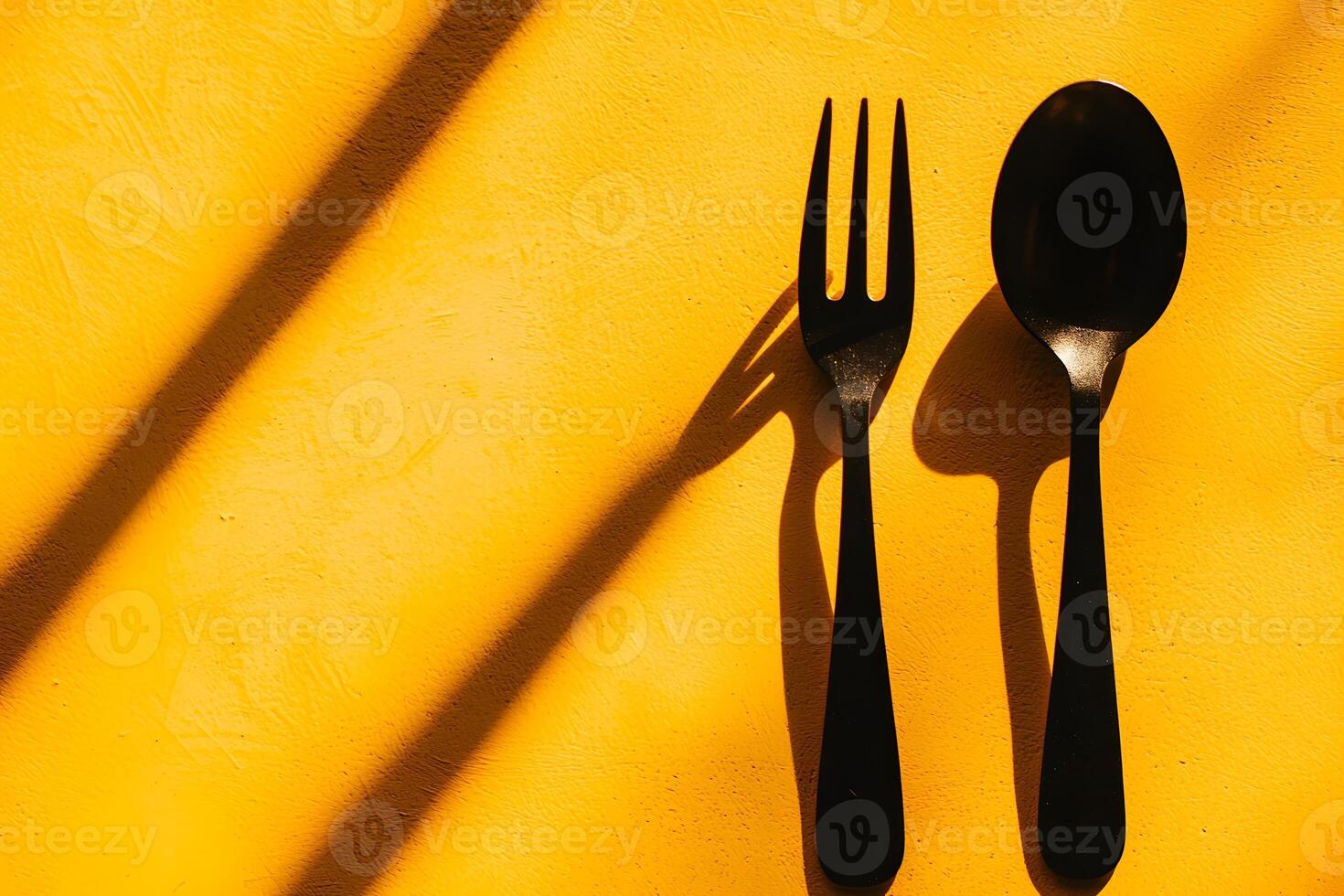 Black Spoon and Fork on Vibrant Yellow Background with Dramatic Sunlight Shadows photo