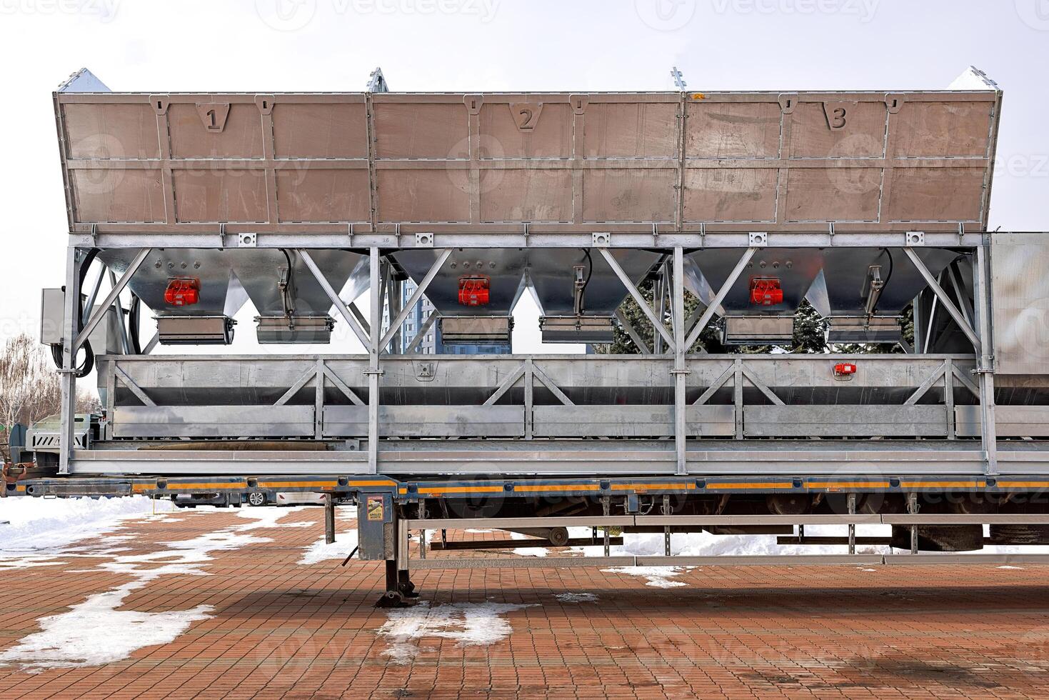 Large metal containers with red vibrators and shakers rest on a trailer in a snowy yard on a cold winter day. photo