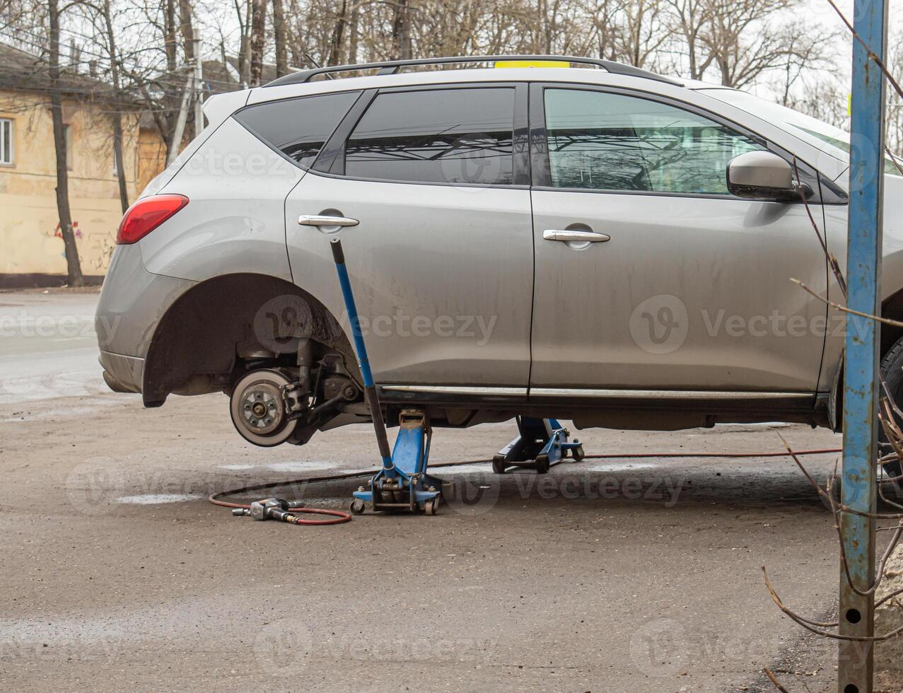 Gray car lifted on jacks removed two rear wheels. High quality photo