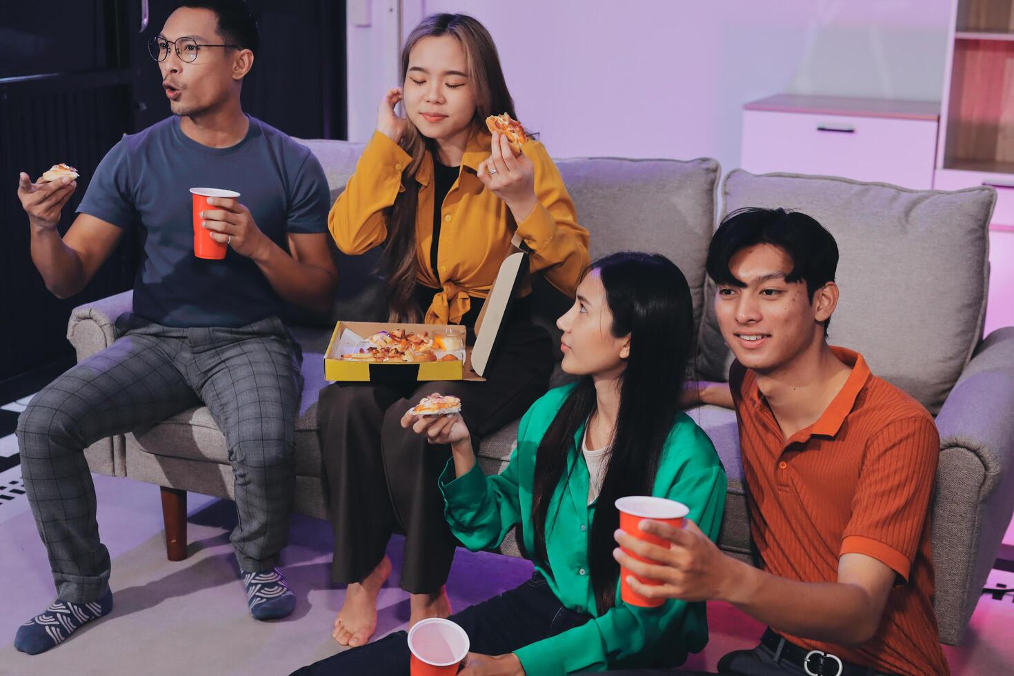 A group of friends sitting on a couch eating pizza and drinking soda photo