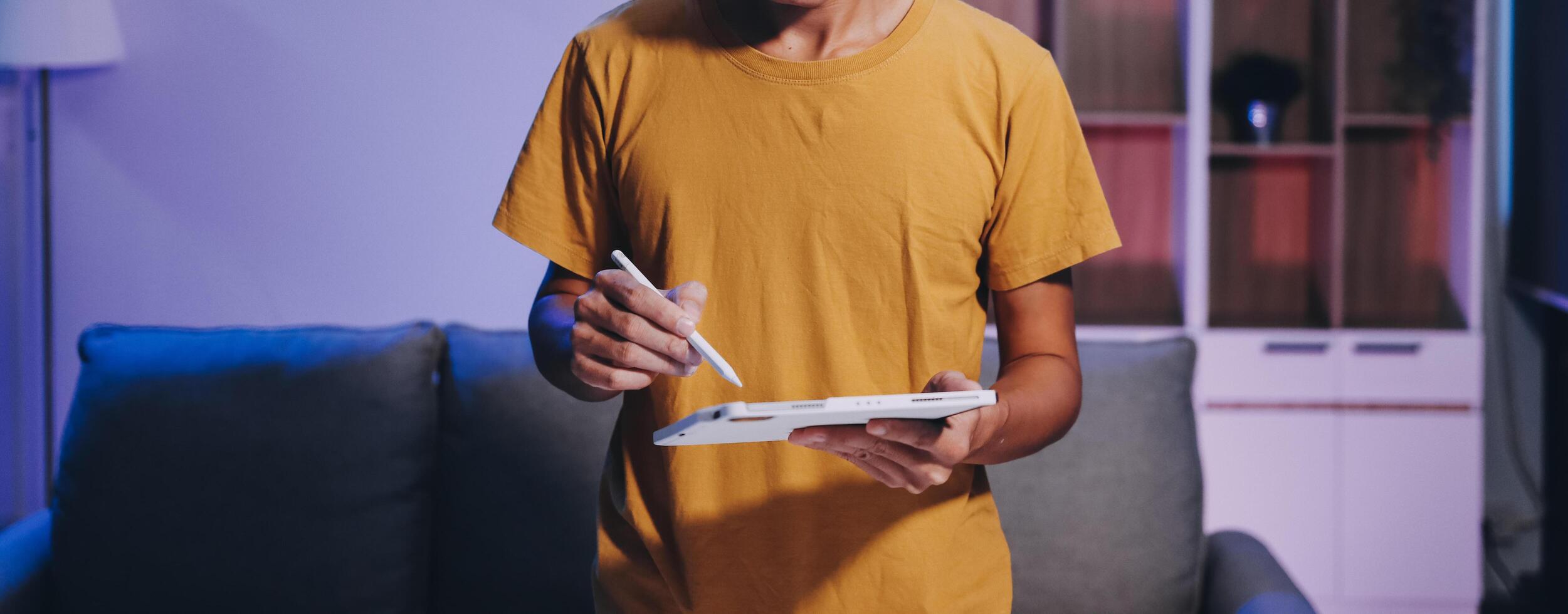 A man holding a tablet while standing in front of a couch photo