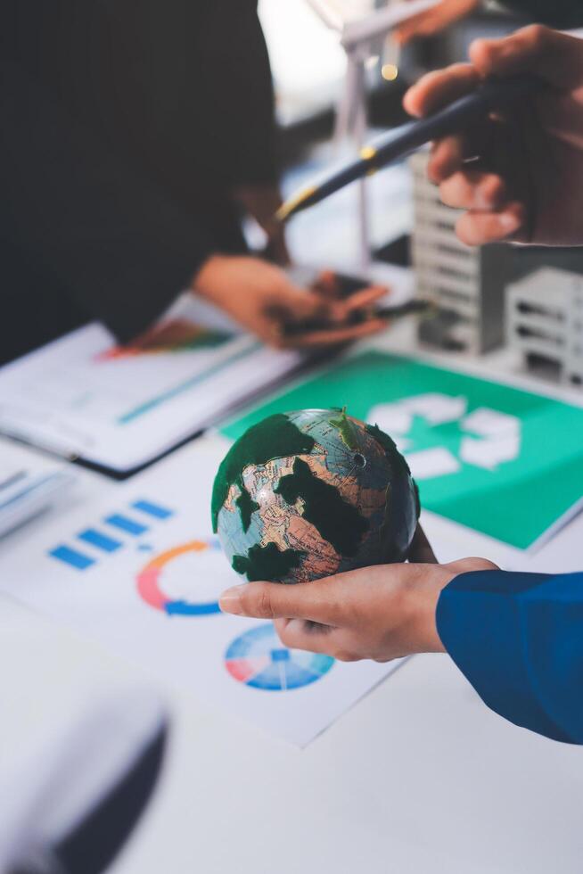 Business people holding a green globe on a table with business documents and graphs photo
