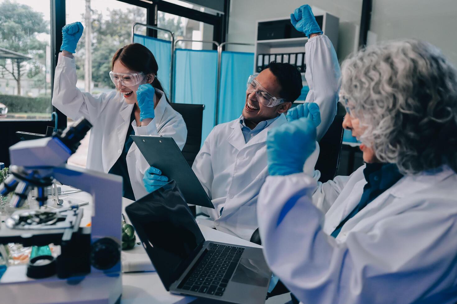 Three people in lab coats and gloves working on a laptop photo
