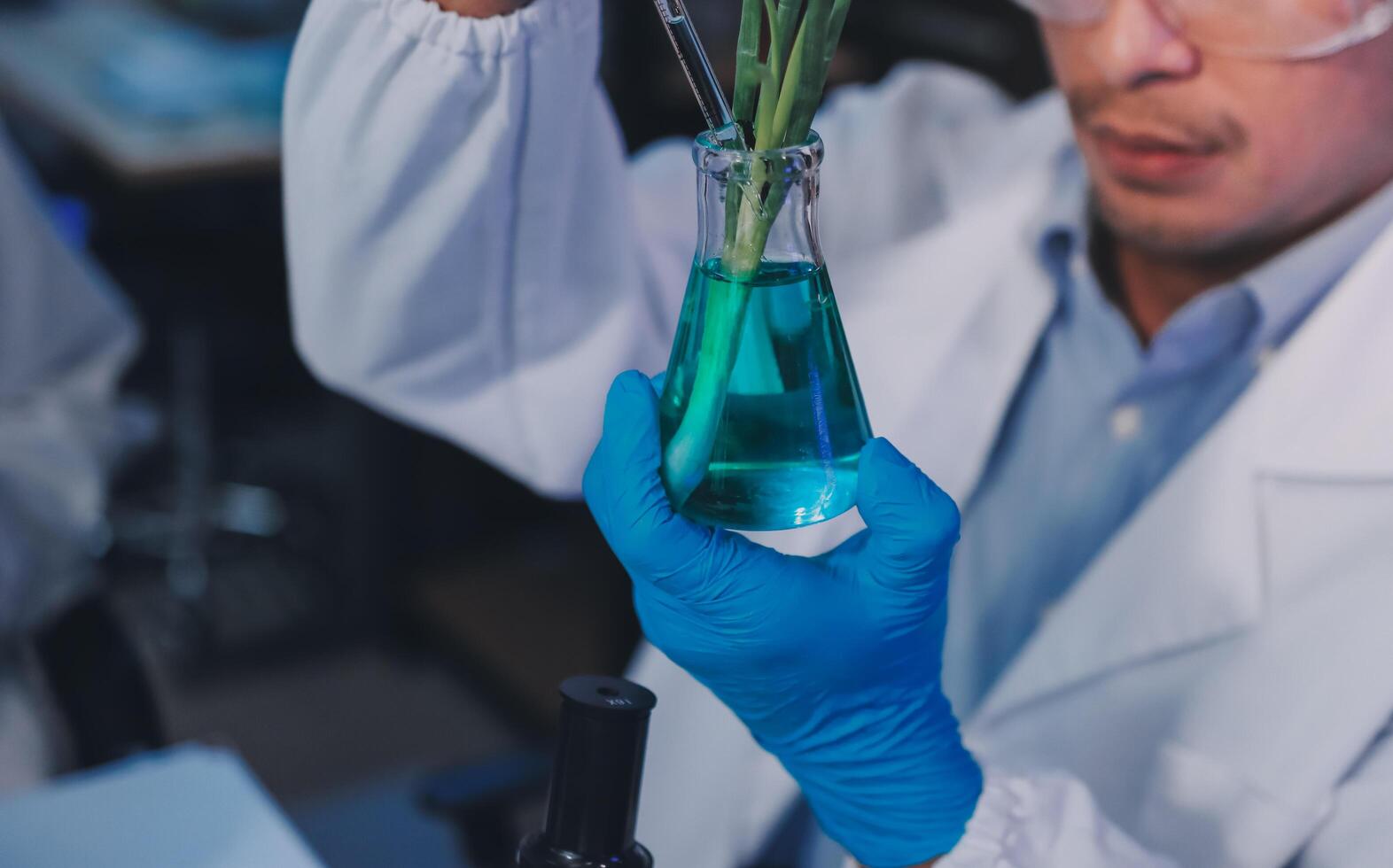 A man in a lab coat holding a plant in a glass photo