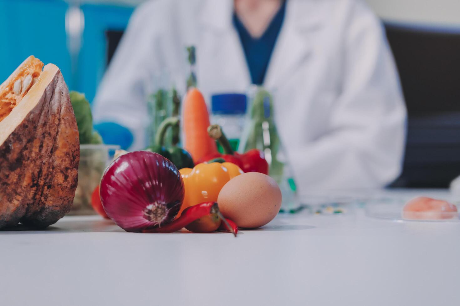 A woman in a lab coat is sitting at a table with a bunch of vegetables photo