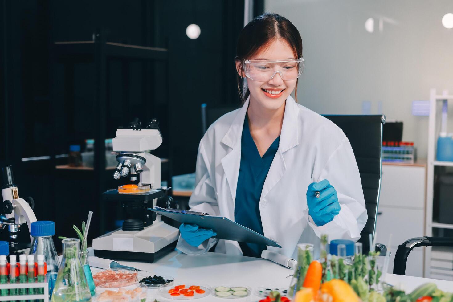 A woman in a lab coat is holding a clipboard and looking at a tablet photo