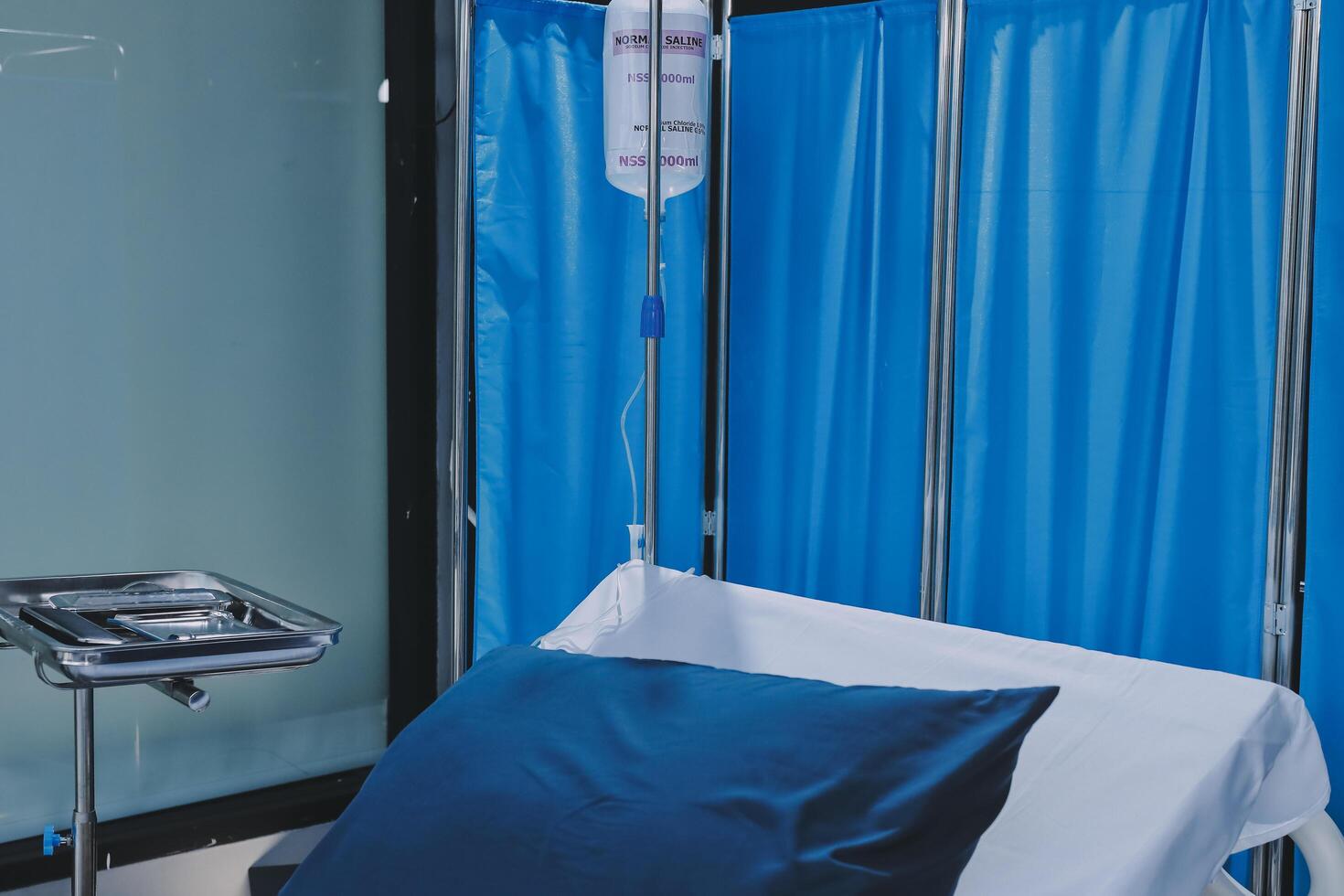 A hospital bed with a drip and a blue curtain photo