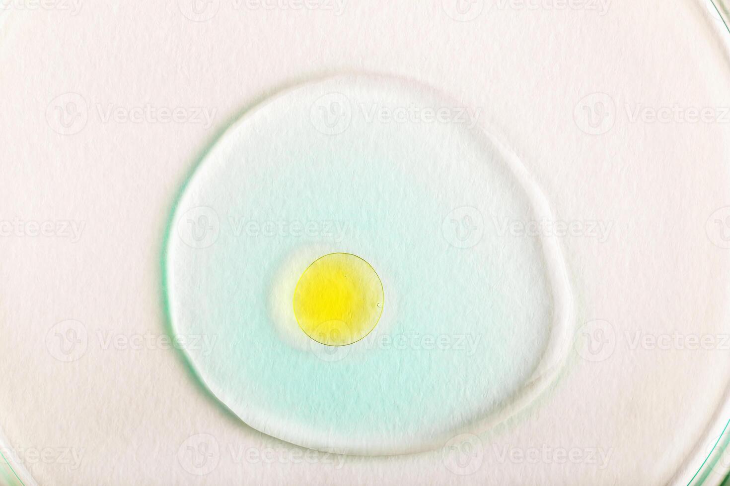 Macro image of vibrant yellow droplet resting in transparent blue gel on white background. Perfect for cosmetic, dermatology or product design concepts. Hydration and nourishment. Yellow oil droplet photo