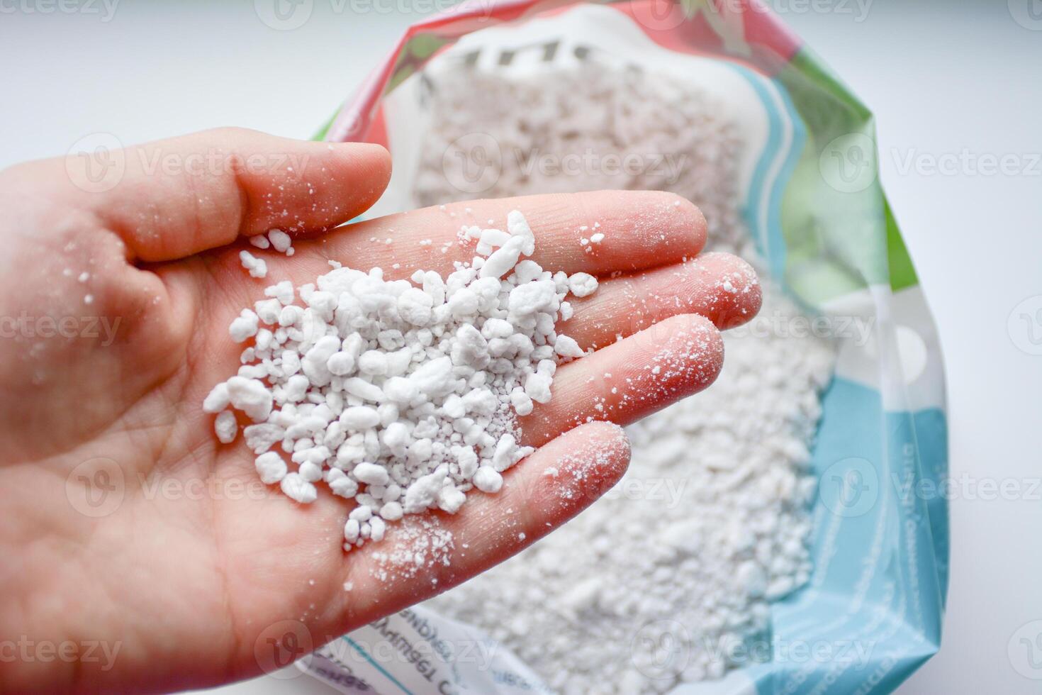 Perlite smaal grains. A hand holds a handful of white perlite against a bag of the material, showcasing its texture. Gardening concept photo