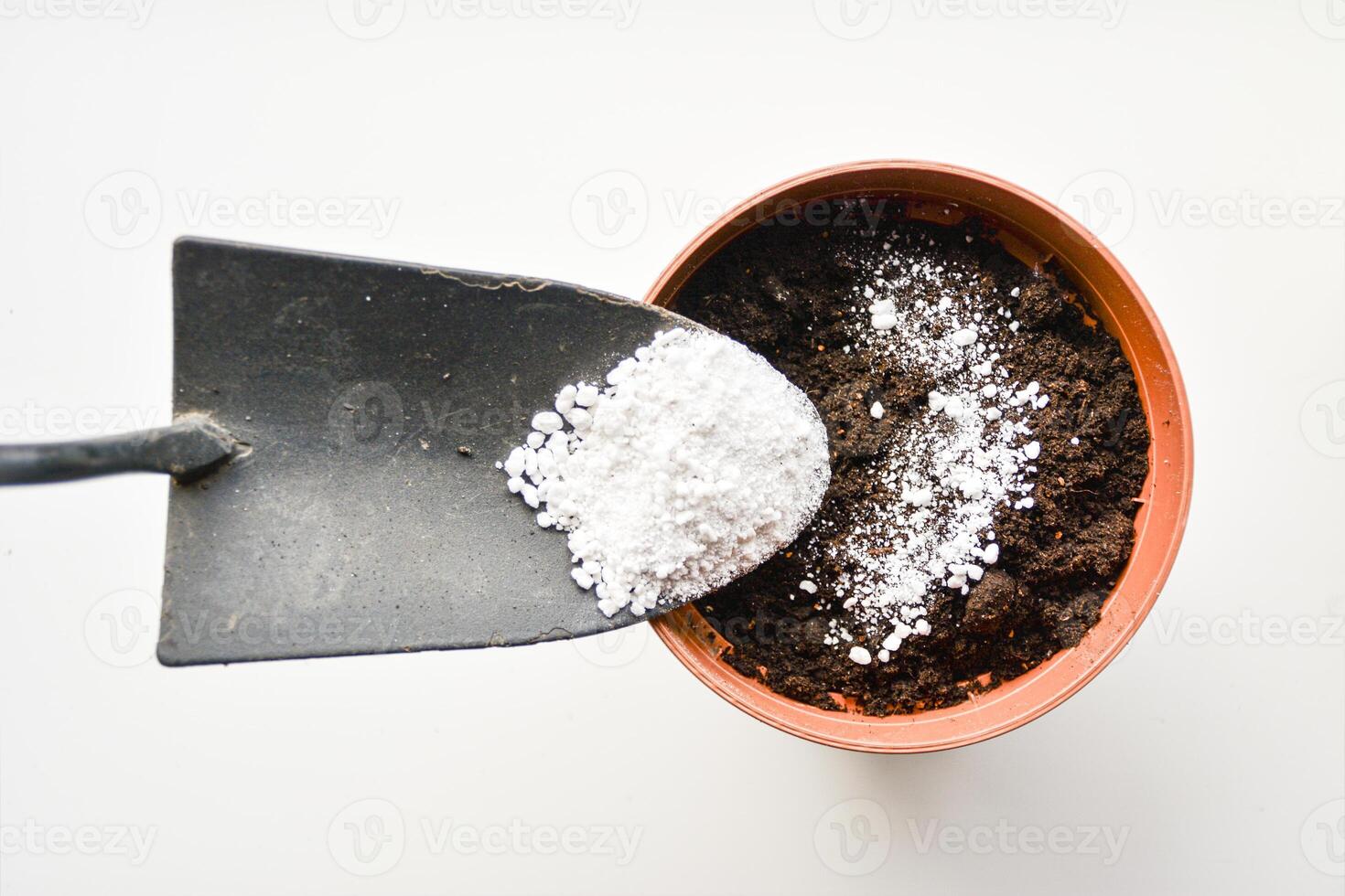 Adding perlite to the soil. Small shovel with perlite above a pot filled with dark soil. Preparing soil for planting, adding nutrients or amendments. Gardening concept photo