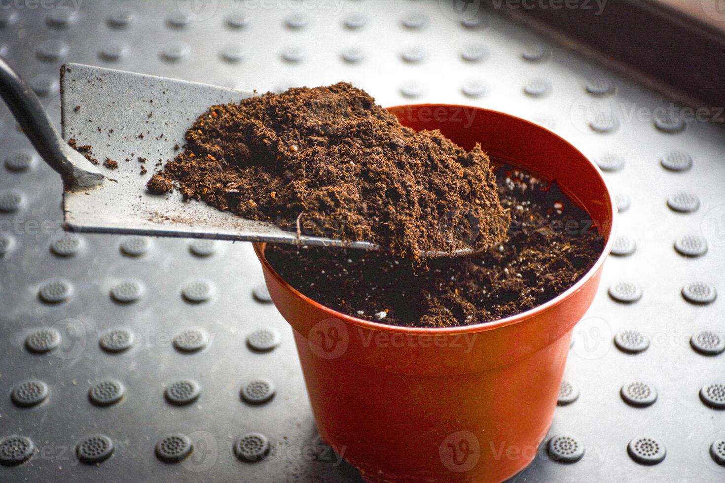 A flower pot filled with dark soil.. A small flower pot and a shovel with fertile earth ready for planting. Gardening concept. photo
