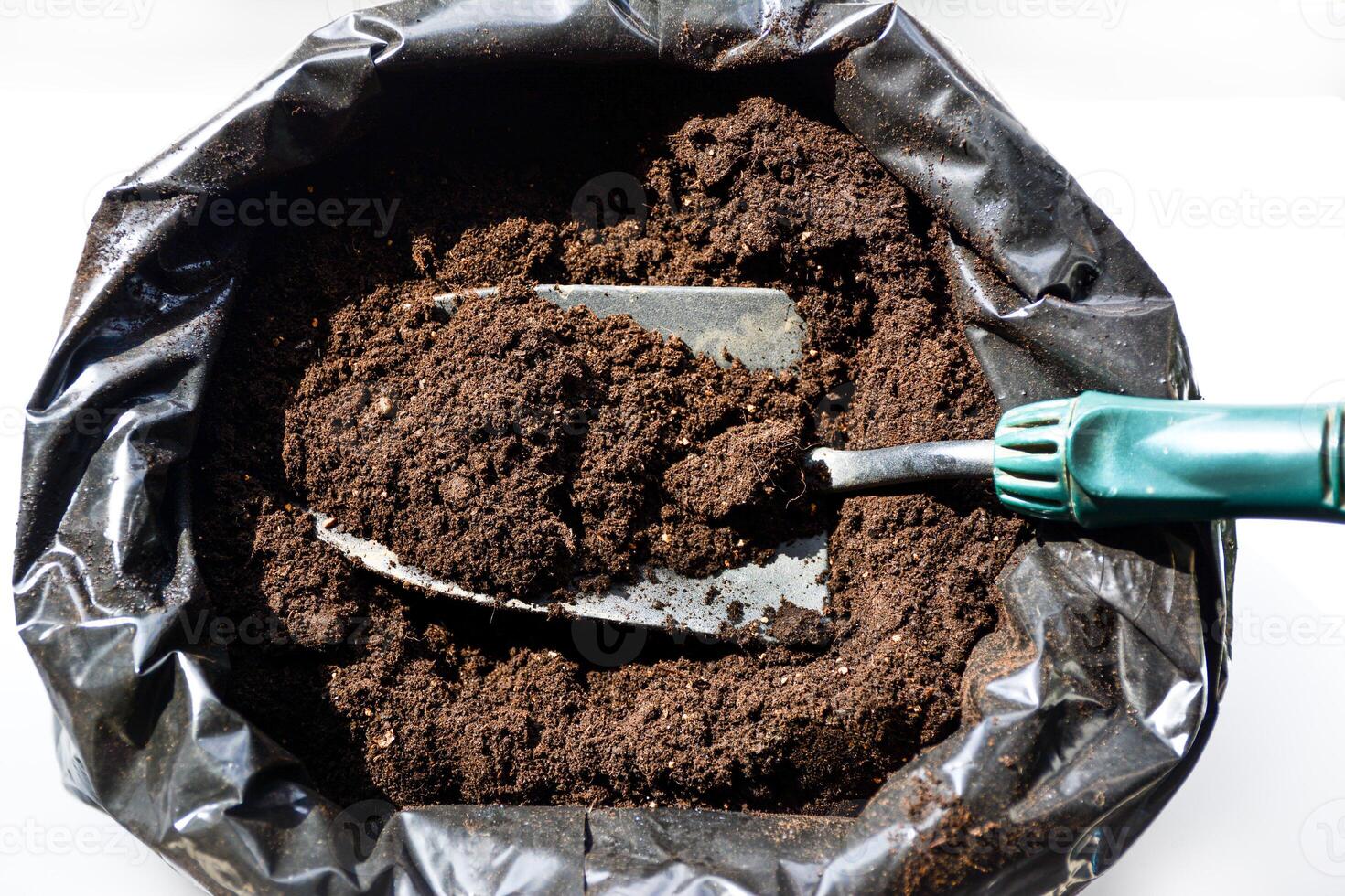 Dark, rich soil in a black plastic container. A bag with fertile soil and a small gardening shovel. Crumbly and fertile soil ready for planting. photo