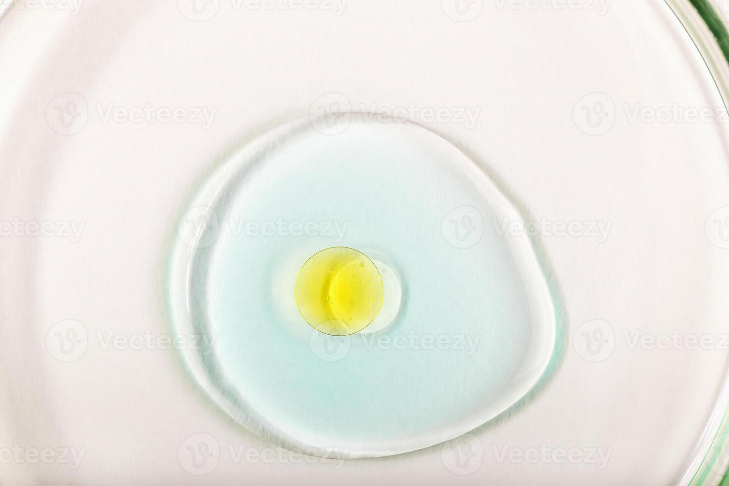 Drop of light blue serum with yellow oil droplet in center on white background. Concept of skincare, pharmaceutical or wellness product. Yellow capsule in blue serum photo