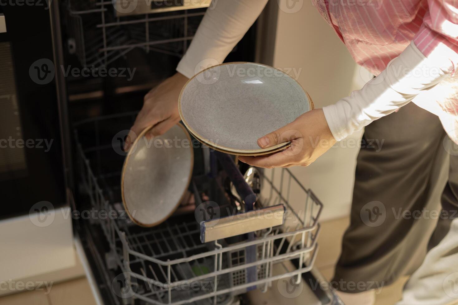 young woman putting plates inside dishwasher, close-up photo