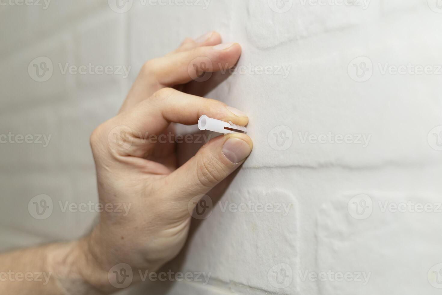 A man's hand holds a dowel for installation near the wall photo
