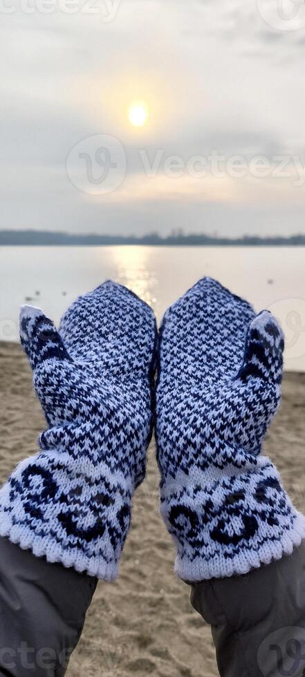 Hands in knitted mittens against the background of a winter landscape and sunset photo