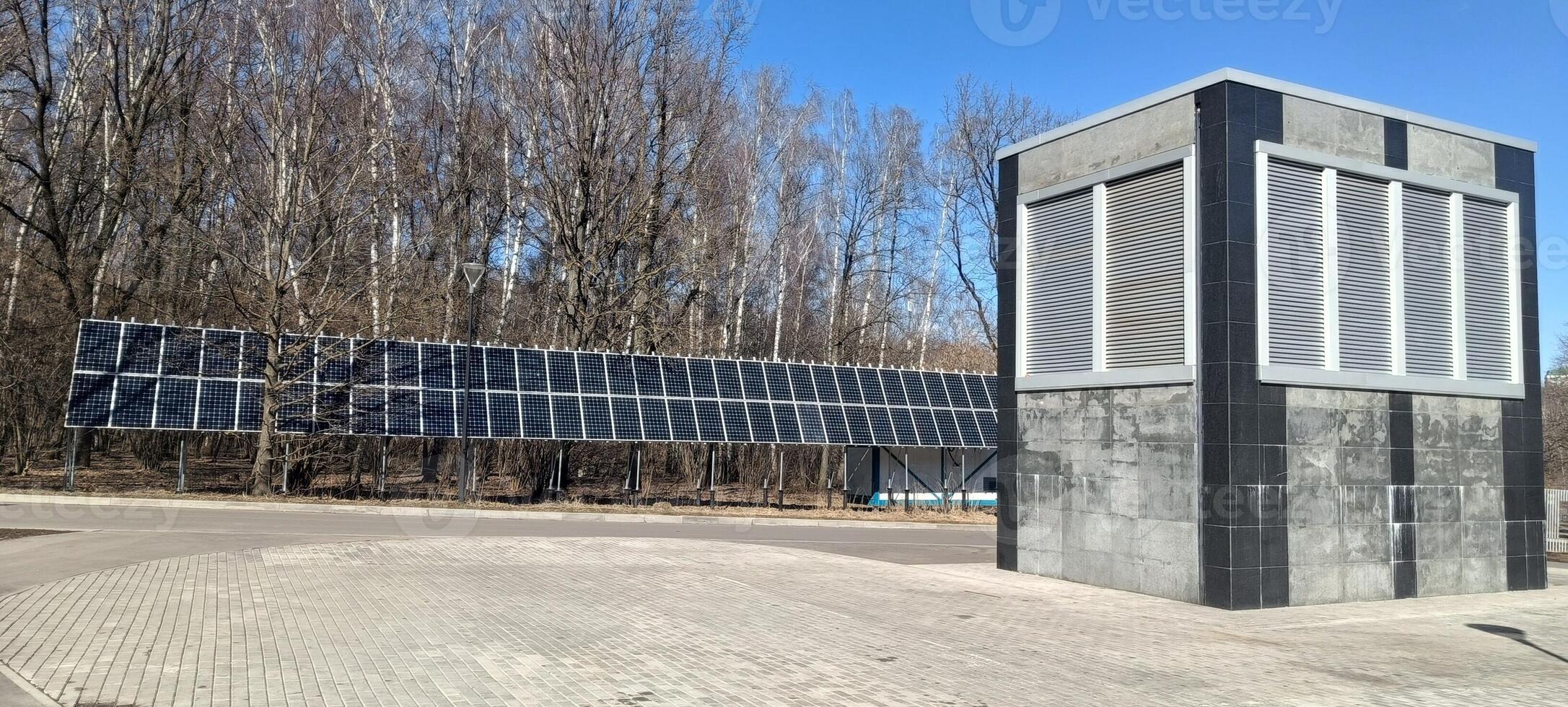 A solar panel array extends alongside a contemporary structure in a forested location. The installation captures sunlight efficiently while blending with nature photo