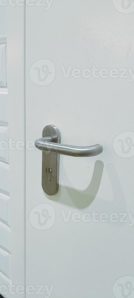 A white door stands against a backdrop of glossy white tiles and black lower wall tiles. The door features a contemporary handle, enhancing the minimalistic decor of the area photo