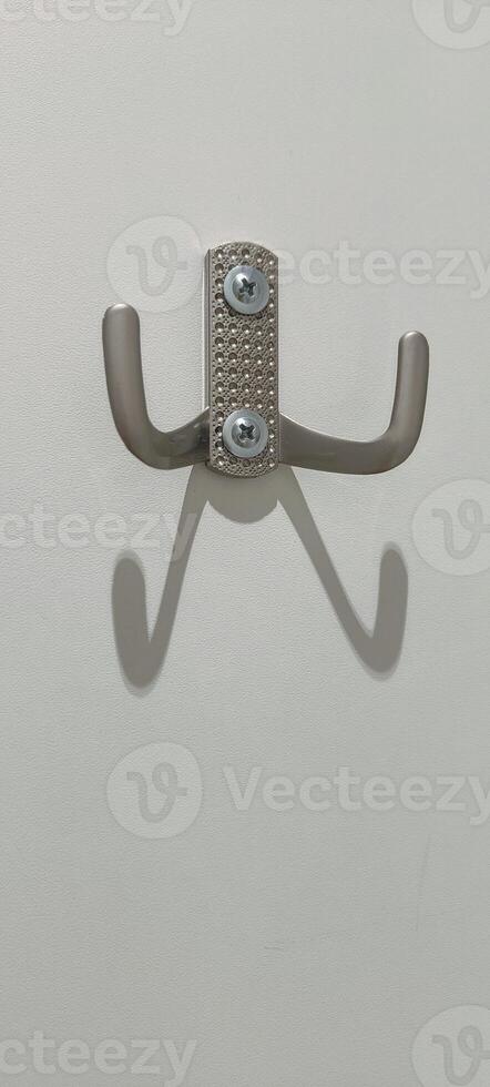 A wall hook designed with a sleek finish is mounted on a white wall. The hooks create interesting shadows, adding a touch of creativity to the minimalist decor. photo