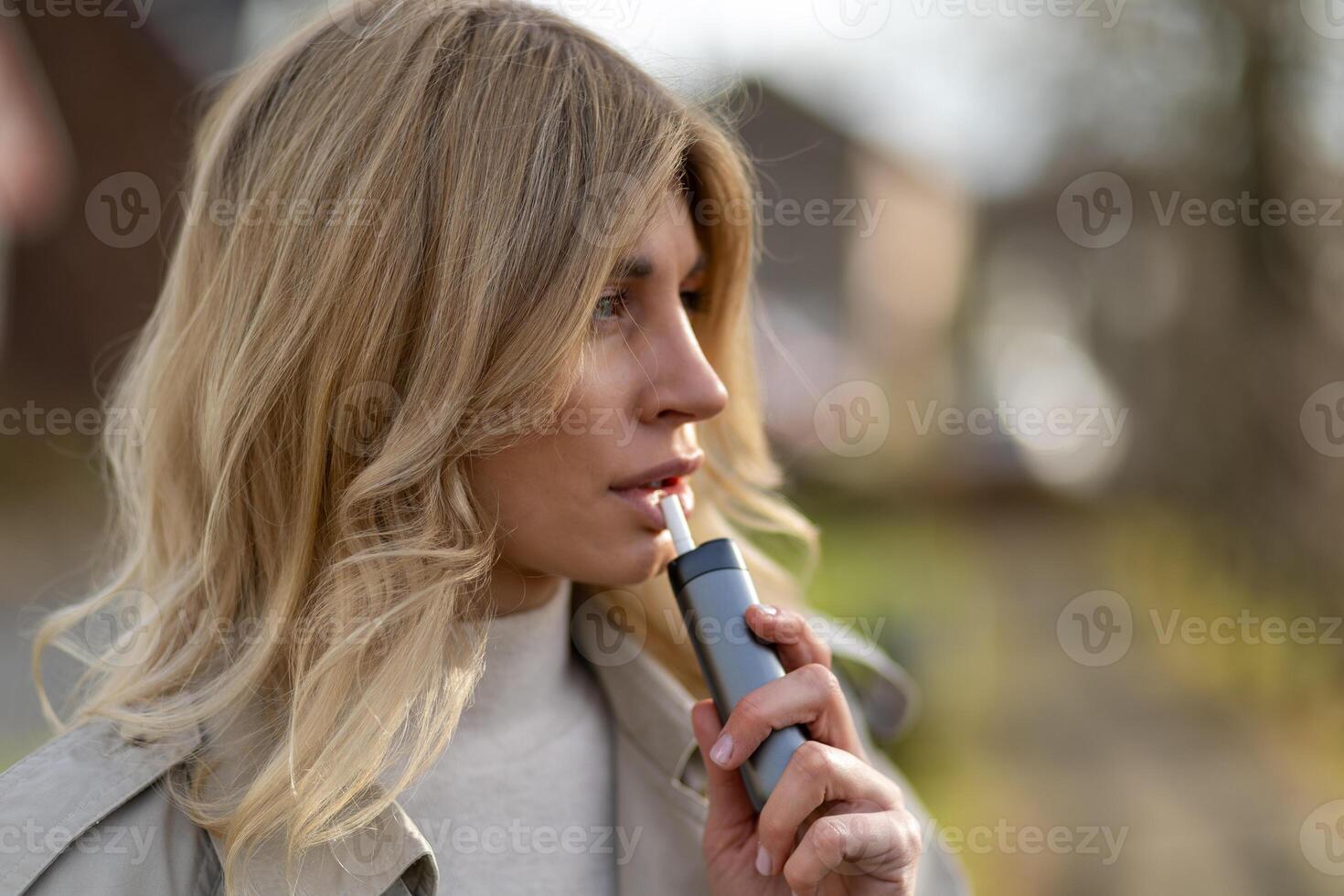 Young woman enjoying a moment outdoors while using a personal vaporizer on a sunny day photo