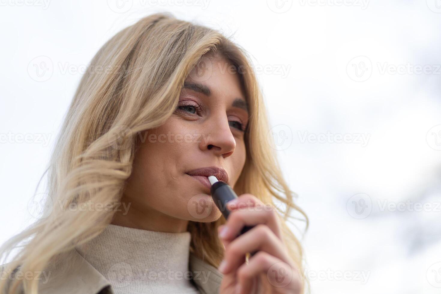 Woman enjoying a vape outdoors on a cloudy day with a relaxed expression photo