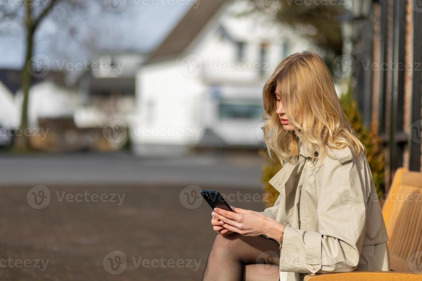 Young woman sitting on a bench in a city while using a smartphone during daytime photo
