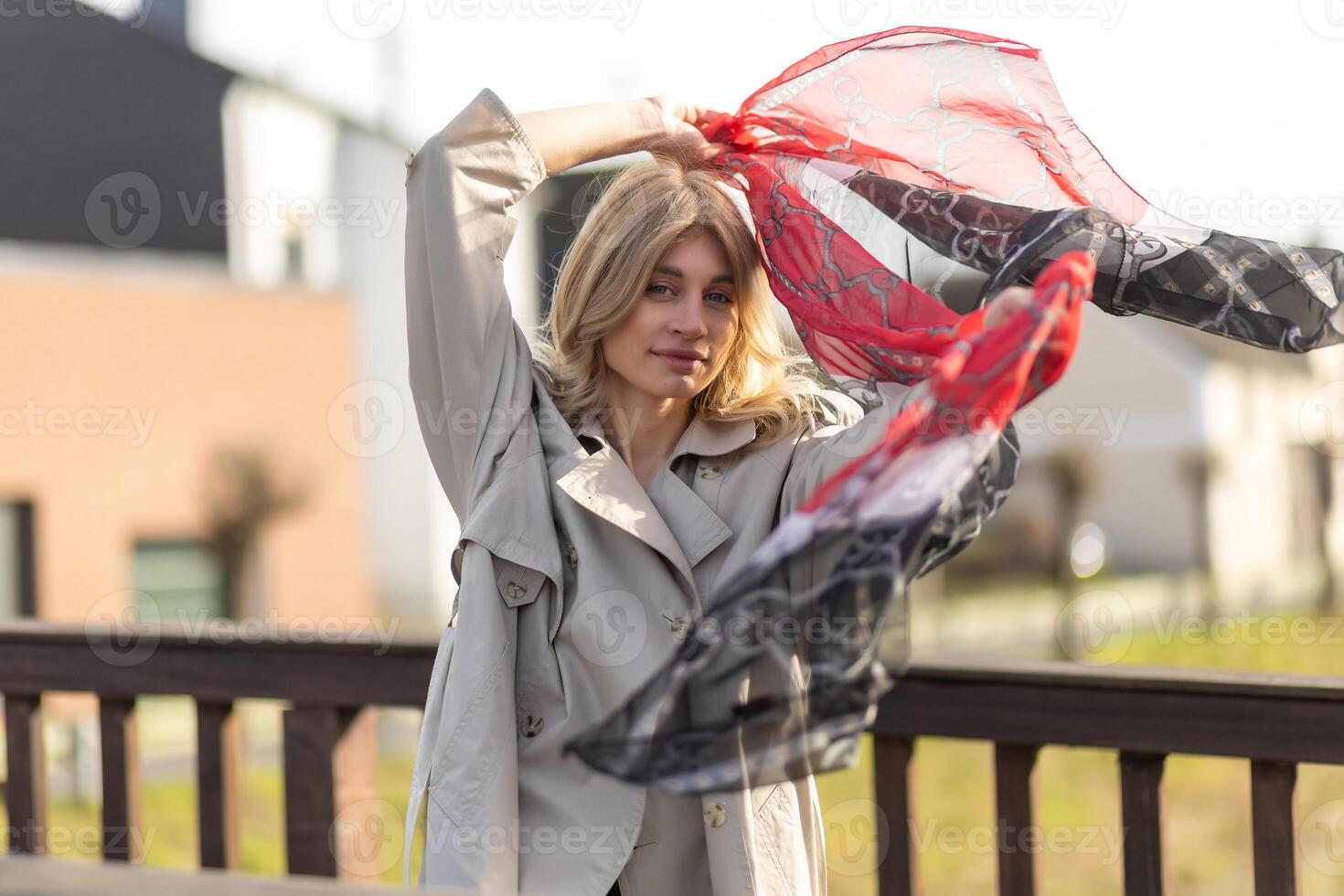 Woman enjoying a sunny day outdoors while playfully waving a scarf near a wooden railing photo