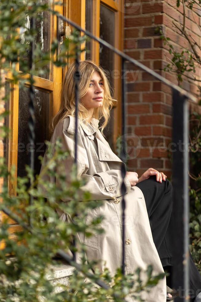 mujer sentado en pasos en un elegante abrigo, disfrutando un pacífico momento en un urbano ajuste durante el tarde tarde foto