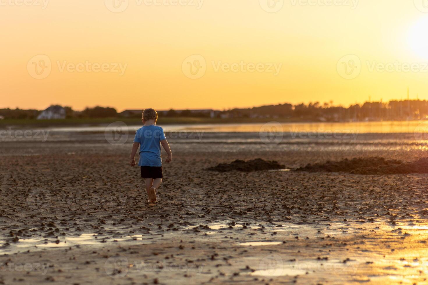 Boy walking on the beach during sunset, exploring the shore at low tide in a tranquil coastal setting photo