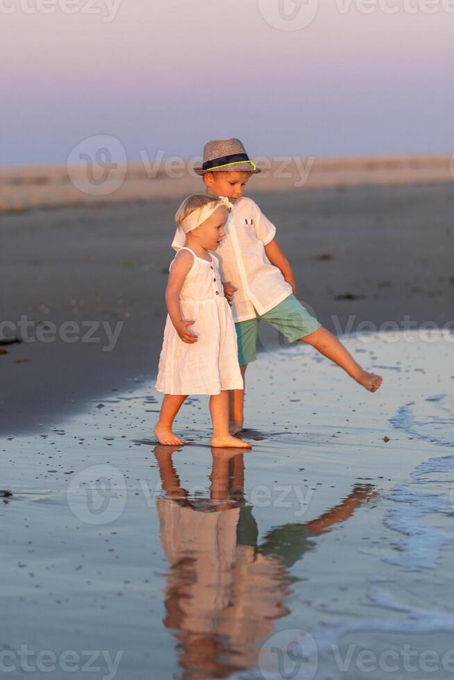 Two children play by the shoreline during sunset, capturing the joy of childhood and nature's beauty photo