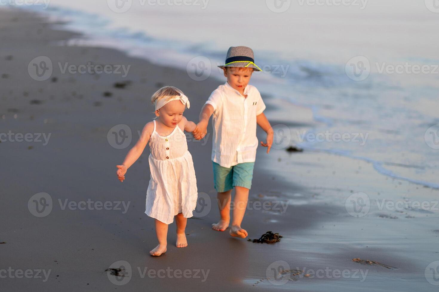 Two children walk hand in hand along the beach at sunset, enjoying a joyful moment by the waves photo