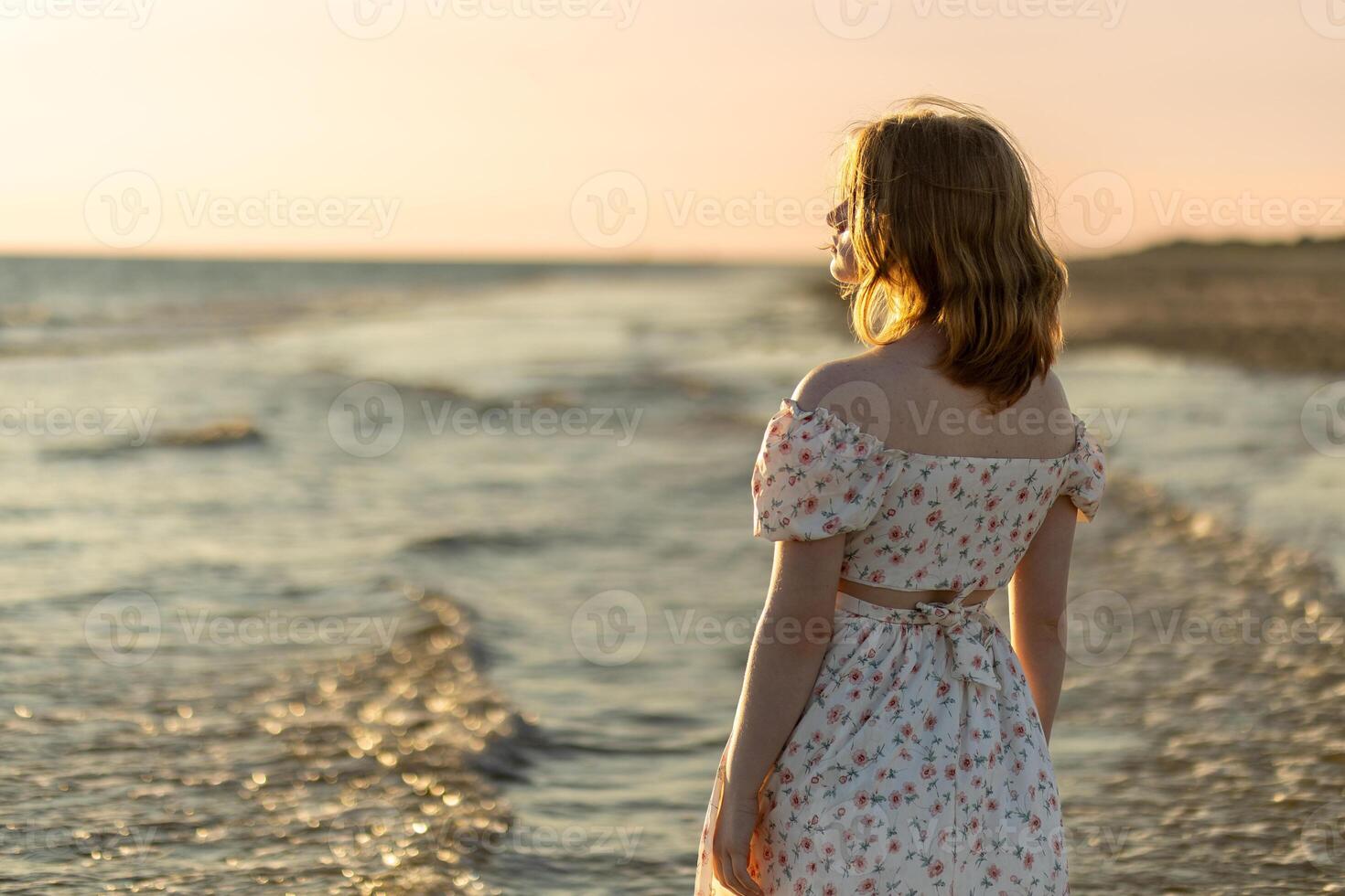 A girl in a floral dress enjoying the sunset by the calm seaside waves in a serene coastal location during summer photo