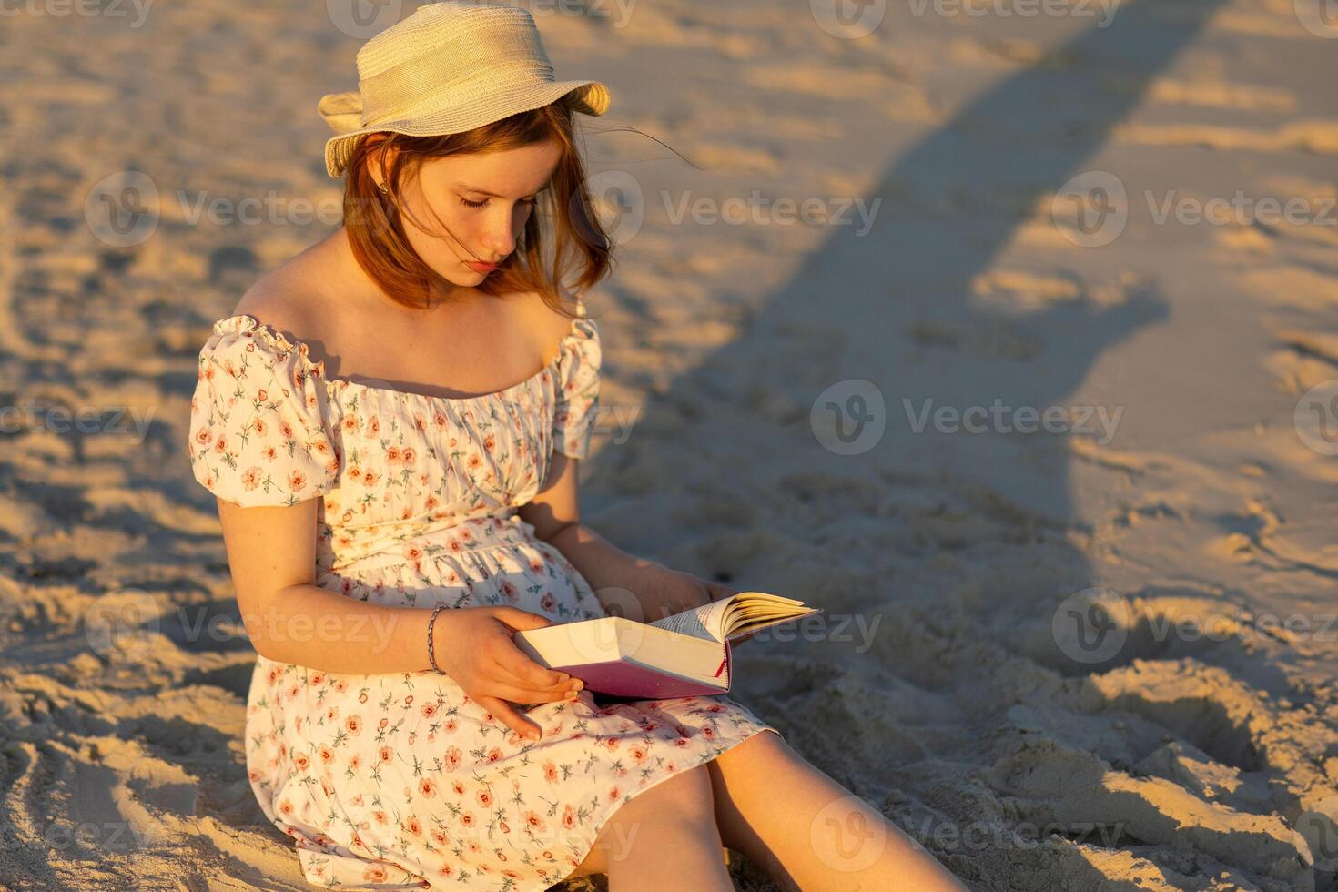 Young woman enjoys reading a book at the beach during sunset on a warm evening photo
