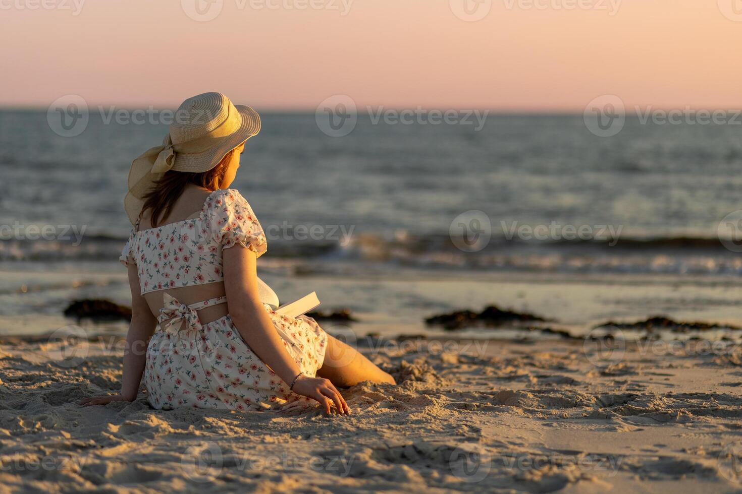 Young woman reading a book on the beach during sunset with soft waves in the background photo