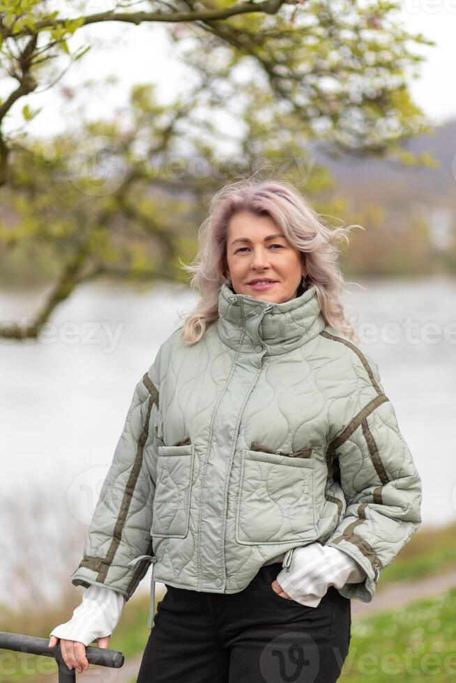 Woman enjoying a serene day by the water, dressed in a cozy jacket during early spring photo