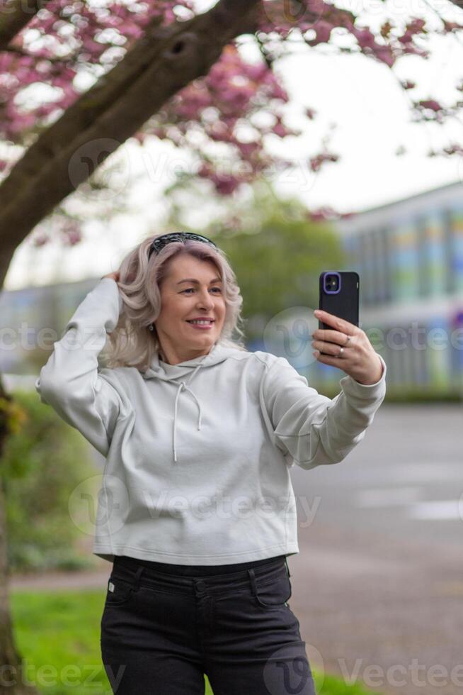 Woman taking a selfie under a blooming tree while smiling in a vibrant outdoor setting photo